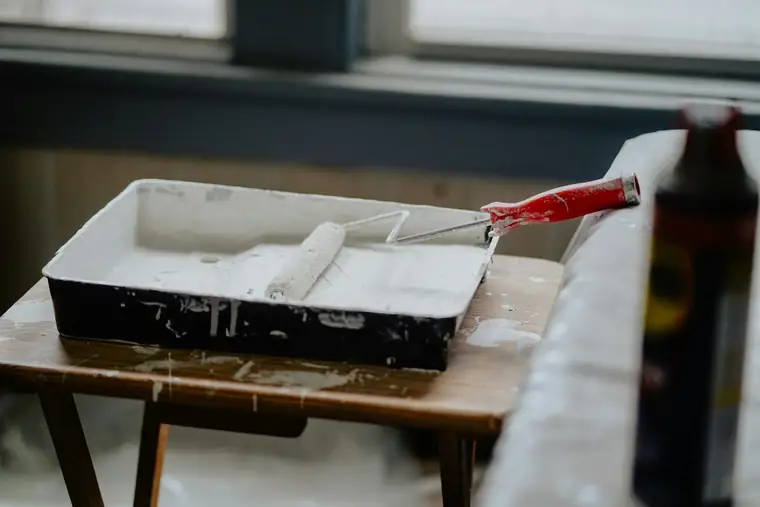 Rouleau posé dans un bac de peinture blanche, sur un escabeau
