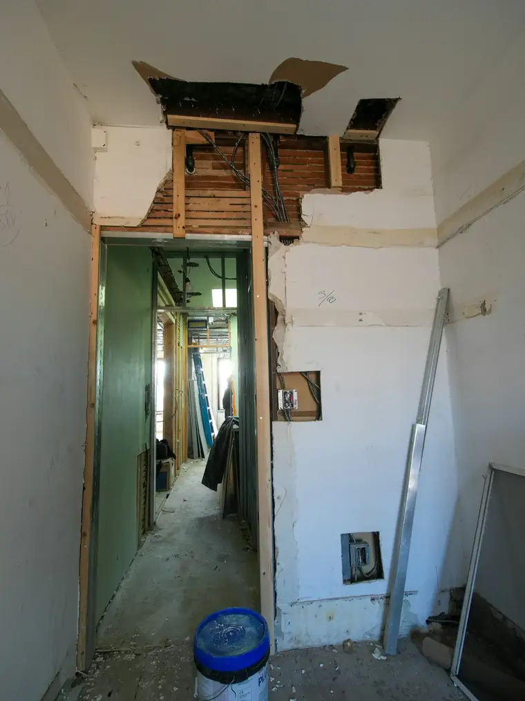 Couloir en rénovation : plafond ouvert, murs repris et passage vers la pièce voisine