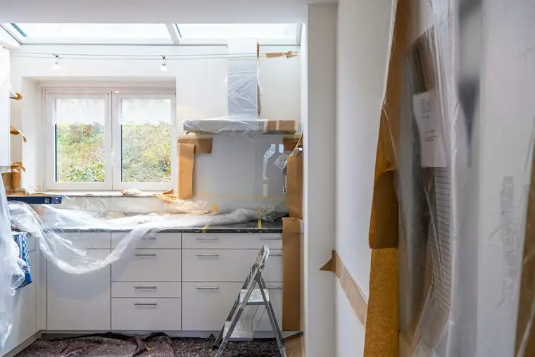 Cuisine en travaux : meubles blancs protégés par du plastique, escabeau au milieu