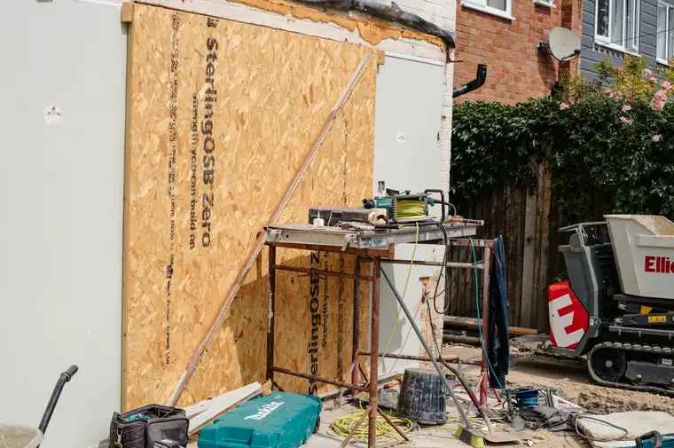 Façade en travaux habillée de panneaux de bois, outils et établi au pied du mur