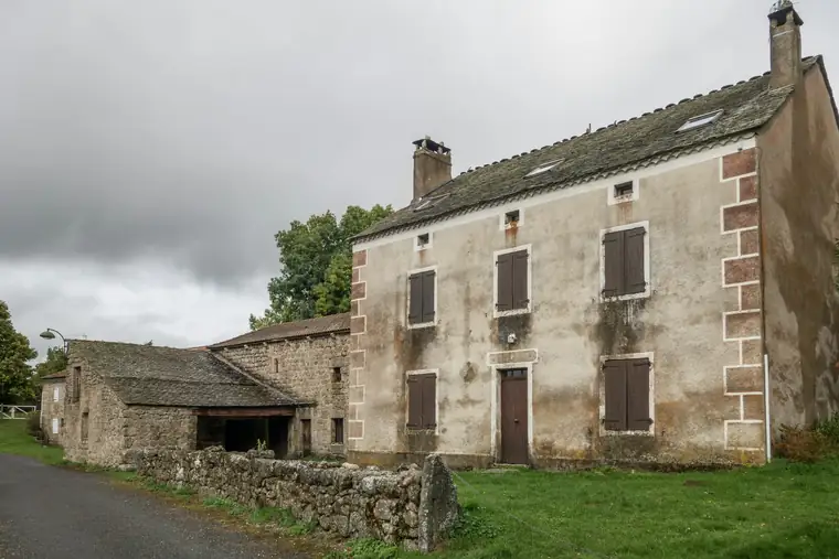 Longère en moellons de pierre aux volets bruns, sous un ciel couvert