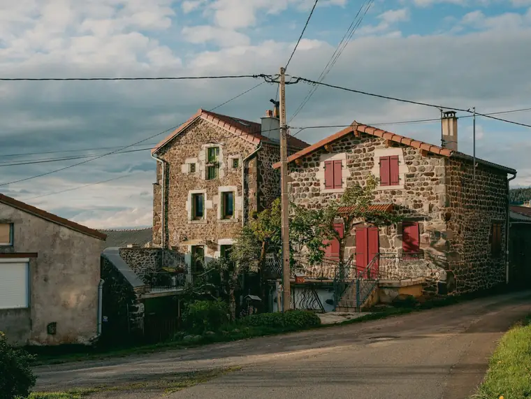 Maisons anciennes en pierre rousse et volets rouges, au bord d’une petite route