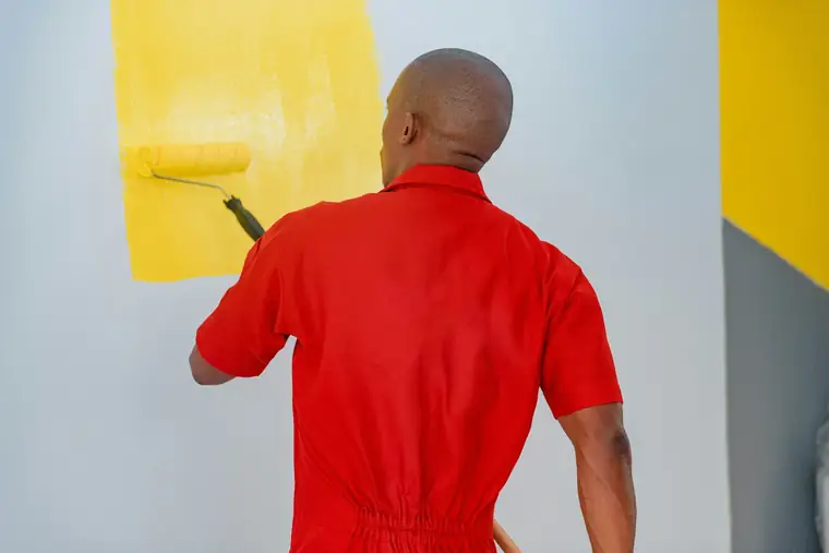 Peintre en tenue rouge qui passe une couche de jaune au rouleau