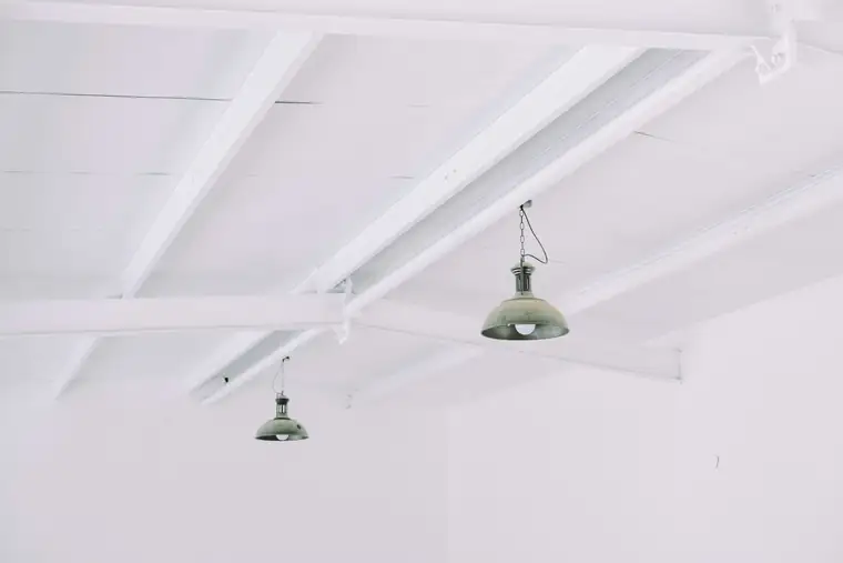 Plafond blanc à poutres peintes et deux suspensions industrielles